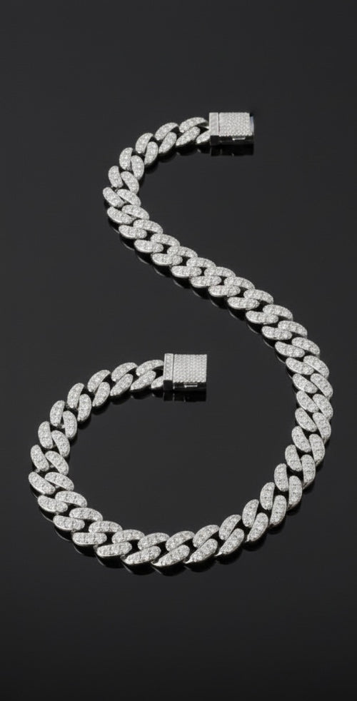The VLTED 10mm Iced Cuban Link Bracelet, encrusted with sparkling stones, is elegantly arranged in an S-shape on a glossy black surface.
