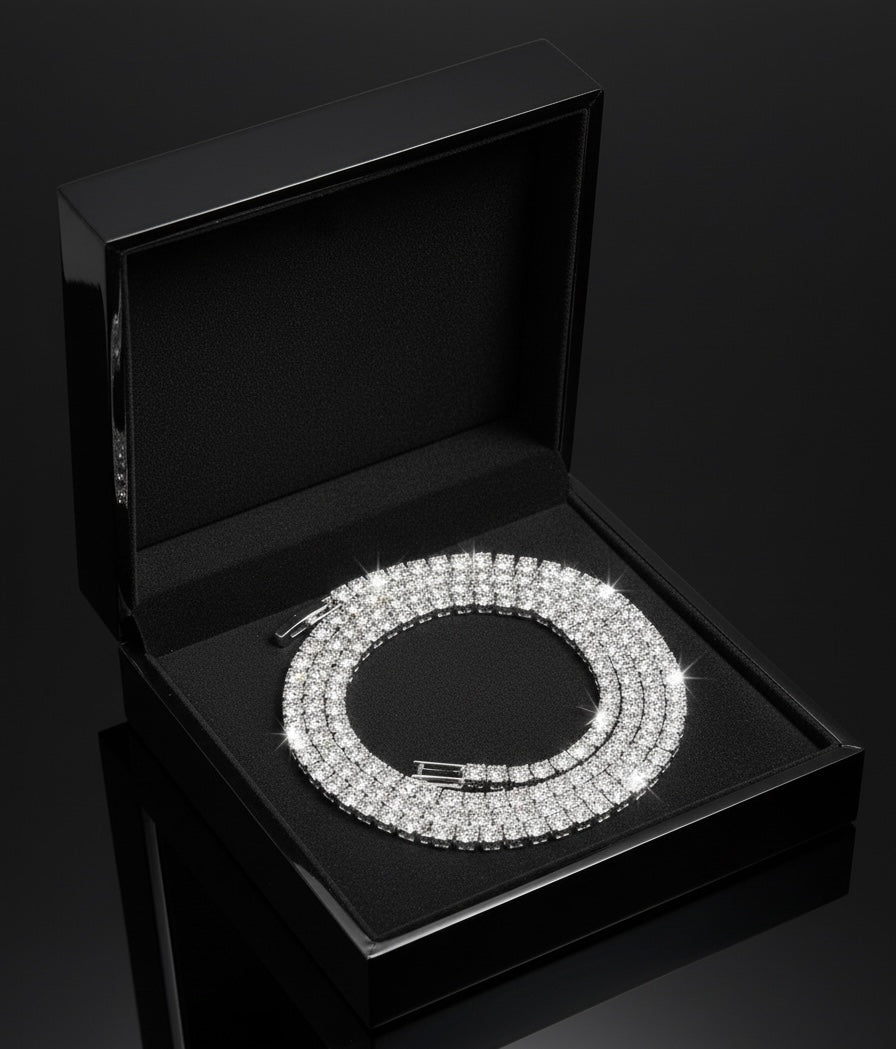 A sparkling diamond tennis bracelet is displayed in an open, black velvet jewelry box on a glossy black surface. The bracelet is neatly coiled and catches the light, creating a brilliant shine.