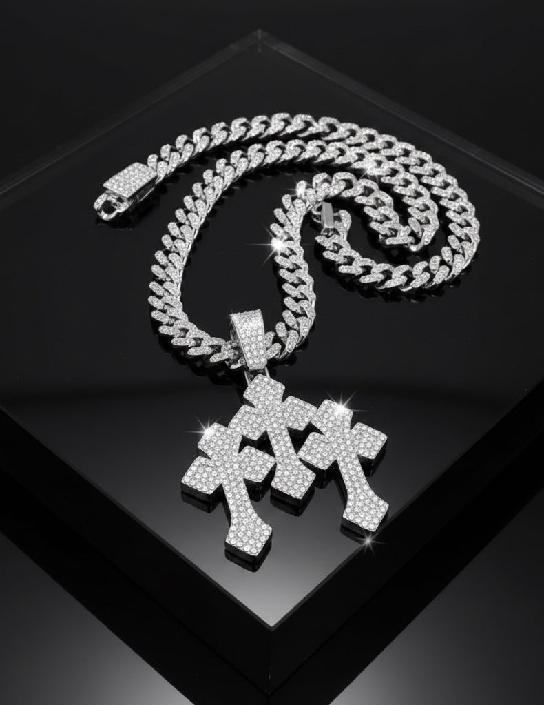 A silver Cuban link chain necklace with two sparkling, diamond-studded cross pendants displayed on a glossy black surface.