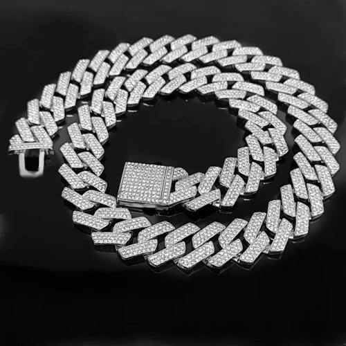 The VLTED 20mm Iced Cuban Link Chain, a silver men's hip hop jewelry piece encrusted with sparkling diamonds, gleams on a glossy black surface.